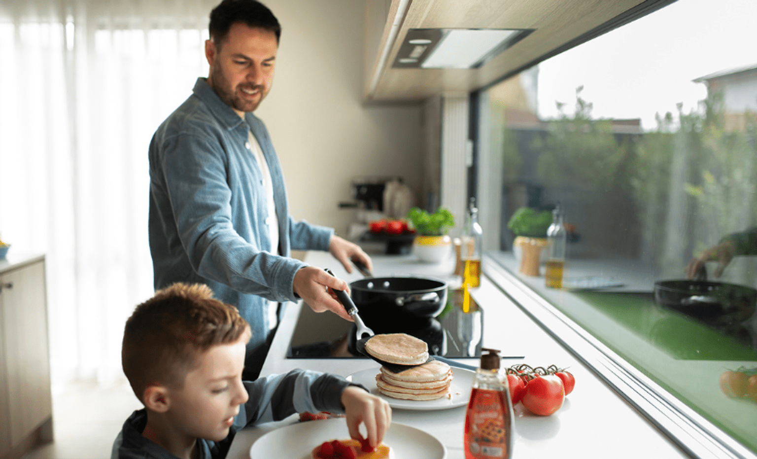 Modern all-electric kitchen with a person using an induction cooktop and a child helping prepare breakfast, showcasing energy-efficient appliances, home electrification, and solar-powered living.