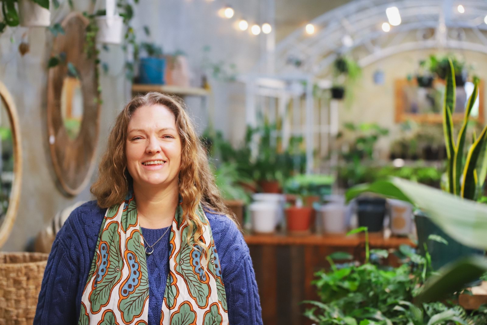 Woman with blonde hair smiling at camera in leafy green cafe