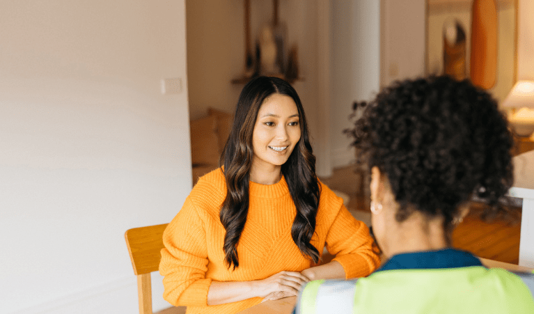 Woman in orange color top sitting at the table and talking to her friend 