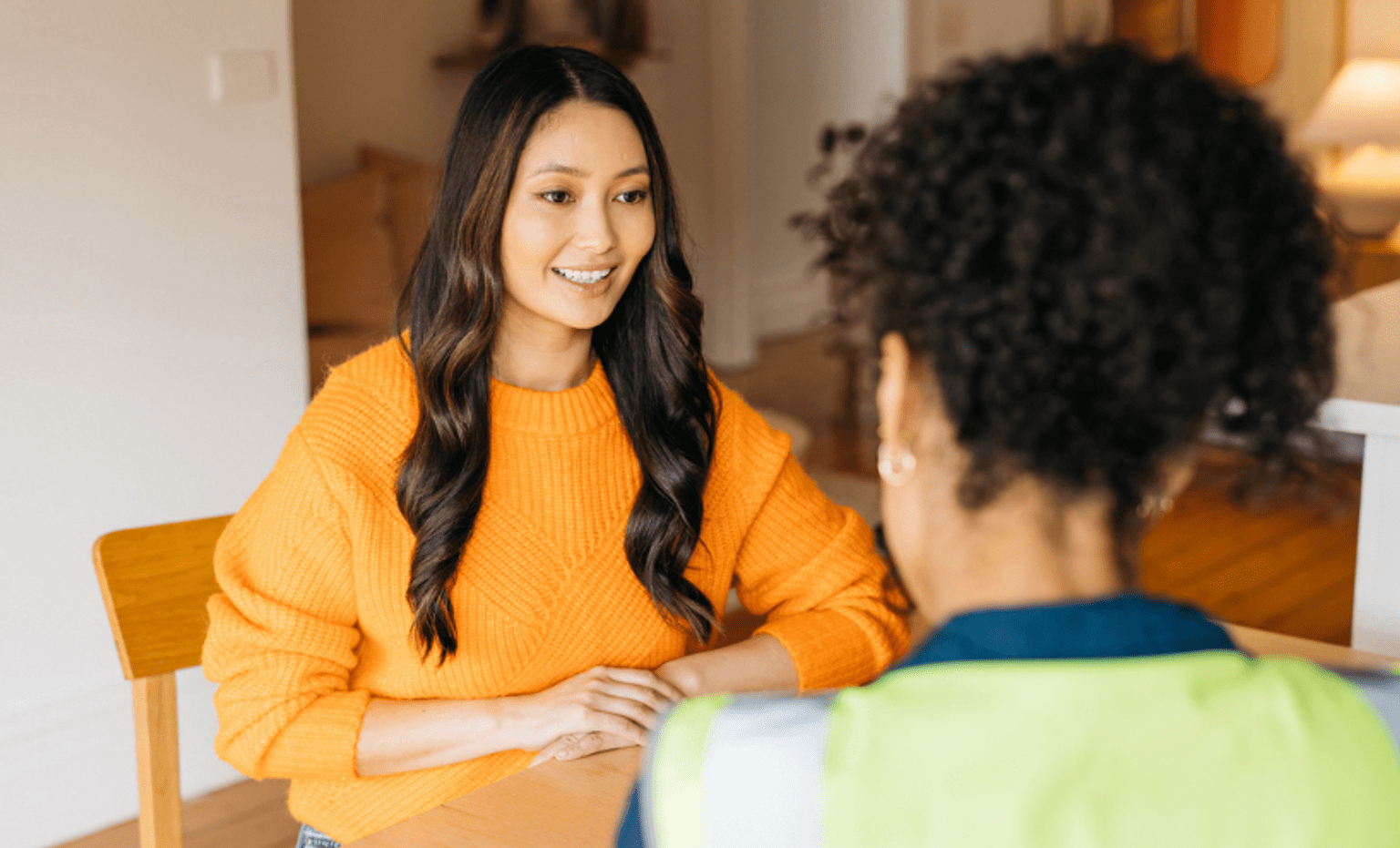 Woman in orange color top sitting at the table and talking to her friend