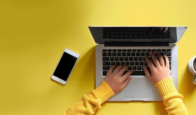 Overhead view of someone's hands typing on a laptop next to a phone